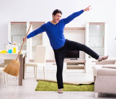 Genç adam yerleri süpürgeyle temizliyor.