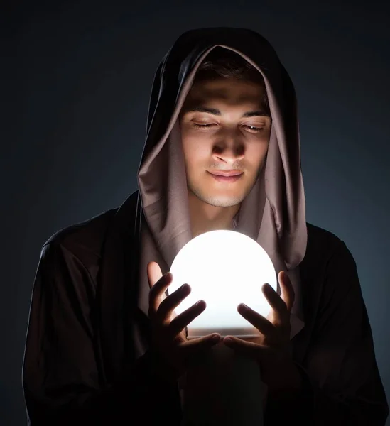 Jovem feiticeiro com bola de cristal no quarto escuro — Fotografia de Stock