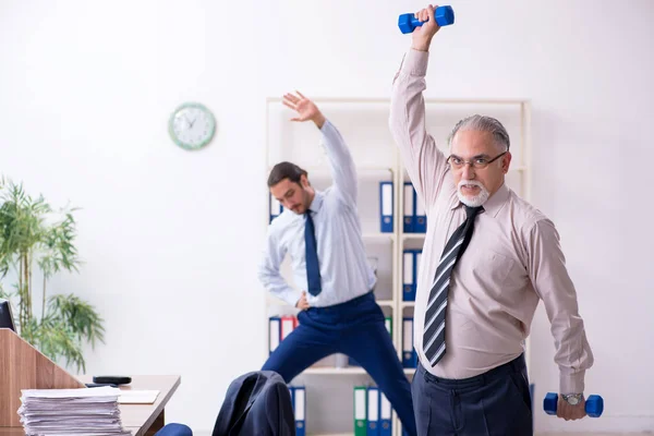 Dois funcionários fazendo exercícios físicos no local de trabalho — Fotografia de Stock
