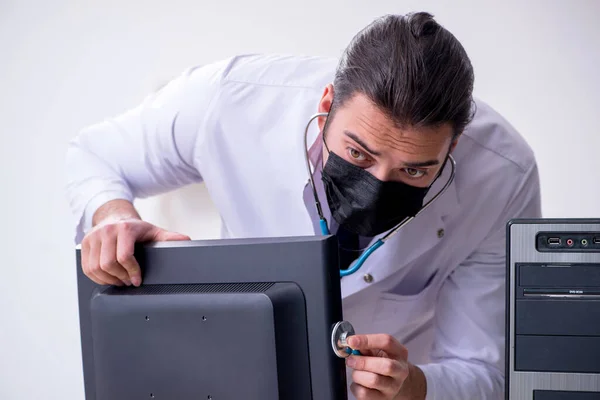 Joven doctor masculino con estetoscopio reparando computadora —  Fotos de Stock