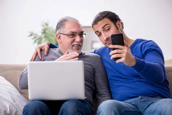 Vader en zoon zitten op de bank met computer — Stockfoto