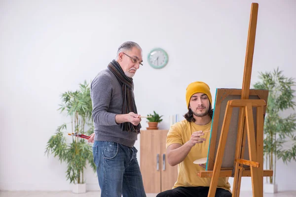 Молодой человек учится у старого художника — стоковое фото