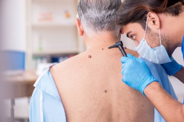 Yaşlı adam genç erkek doktor dermatoloğu ziyaret ediyor.
