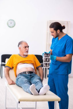 Yaşlı adam genç erkek doktoru ziyaret ediyor.