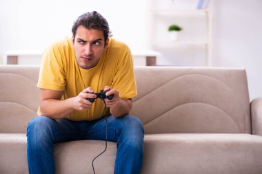 Genç adam evde joystick oynuyor.