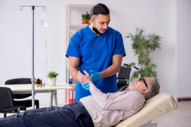 Yaşlı hasta damar içi tedavi için genç erkek doktoru ziyaret ediyor.