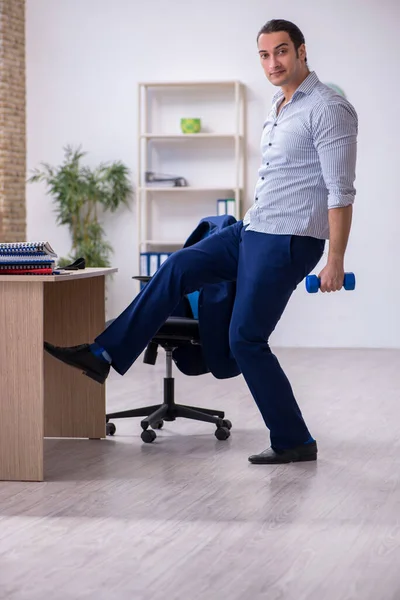 Jonge knappe mannelijke werknemer doet oefeningen in het kantoor — Stockfoto