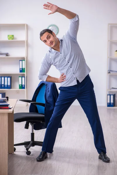 Young handsome male employee doing exercises in the office — Stock Photo, Image