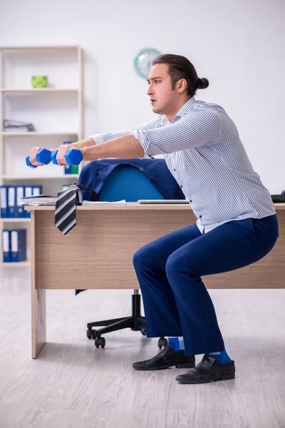 Young handsome male employee doing exercises in the office — Stock Photo, Image