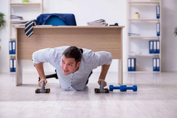 Joven empleado masculino guapo haciendo ejercicios en la oficina —  Fotos de Stock