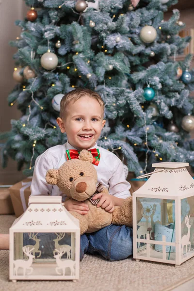 彼のお気に入りのおもちゃとうれしそうな少年がクリスマス ツリーの下に座っています — ストック写真