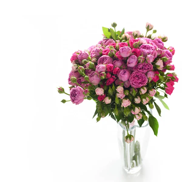 Floral composition of pink and purple roses in glass vase isolated on white background