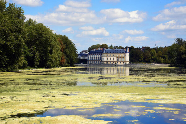 Chateau de Rambouillet castle near river on background of blue sky and white clouds, France.