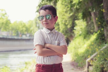 Güneş gözlüğü takan çocuk parkta çapraz kollarla poz verdi