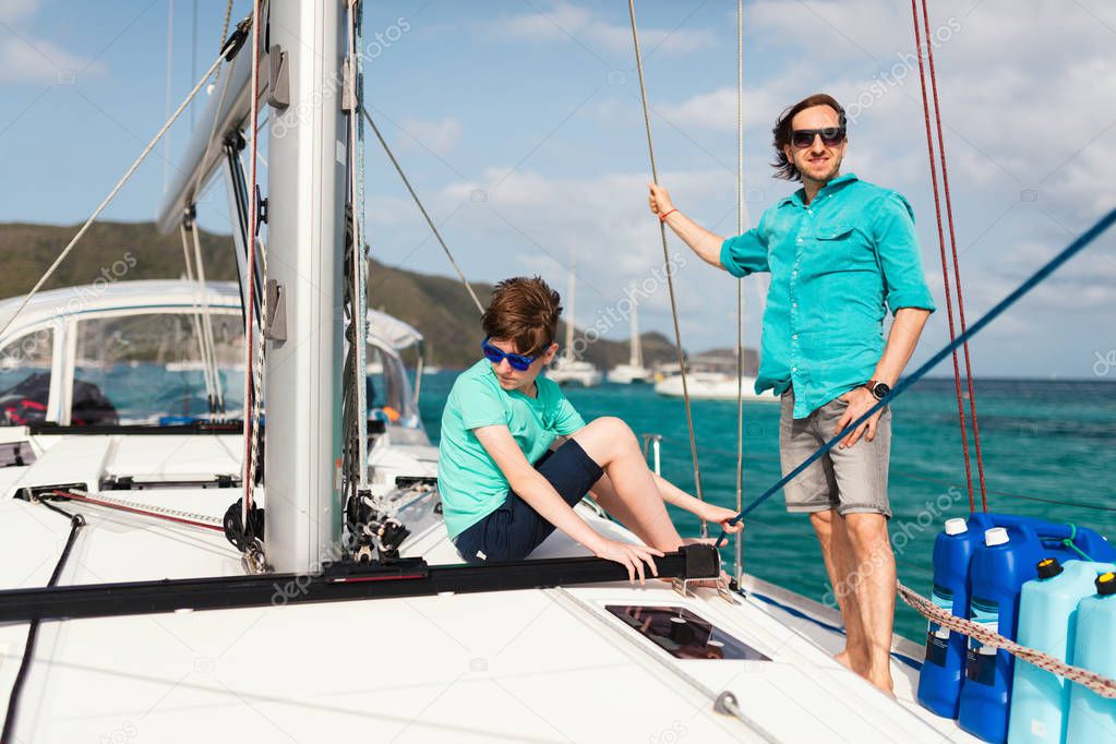 Father and his teenager son on board of sailing yacht having summer travel adventure