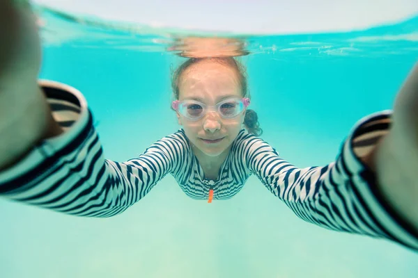 Split underwater photo of cute girl having fun in a tropical ocean taking selfie