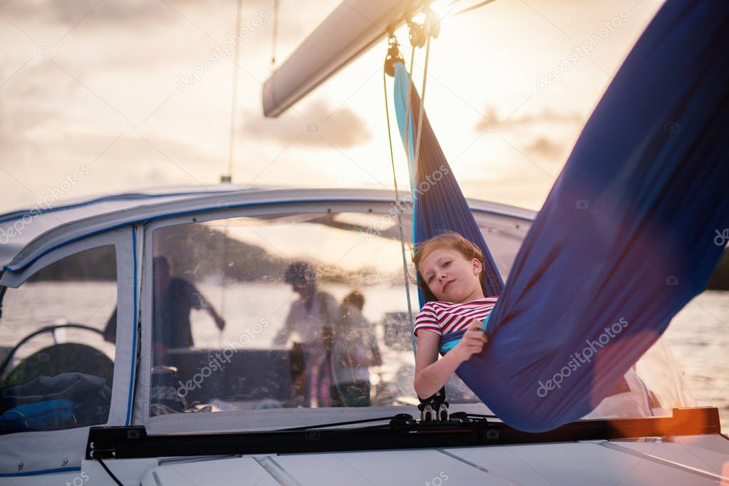 Cute girl enjoying sunset relaxing in the hammock set on the sail boat while sailing in the open sea