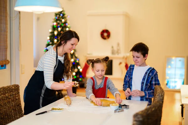 母亲和孩子在圣诞节前夜烘烤饼干在家的家庭 装饰精美的房间 圣诞树及背景灯 — 图库照片