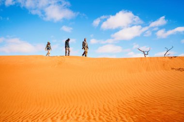 Family of father and two kids climbing up red sand dune in Namib desert clipart