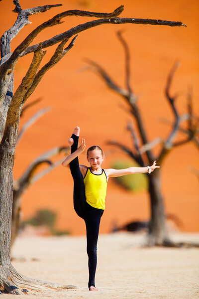 Adorable young girl among dead camelthorn trees surrounded by red dunes in Deadvlei in Namibia