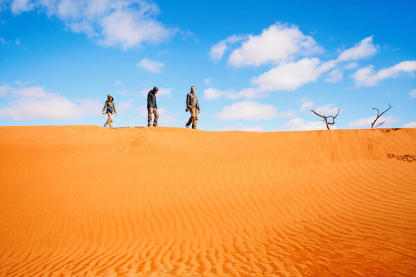 Family of father and two kids climbing up red sand dune in Namib desert