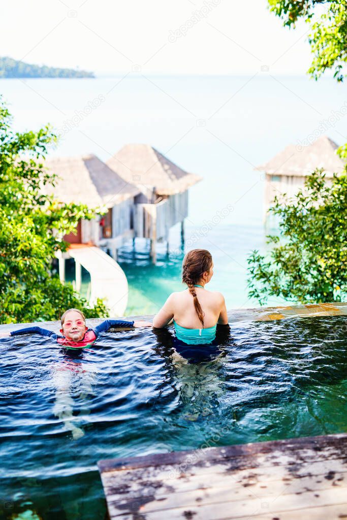 Happy family mother and daughter at outdoors infinity swimming pool enjoying views
