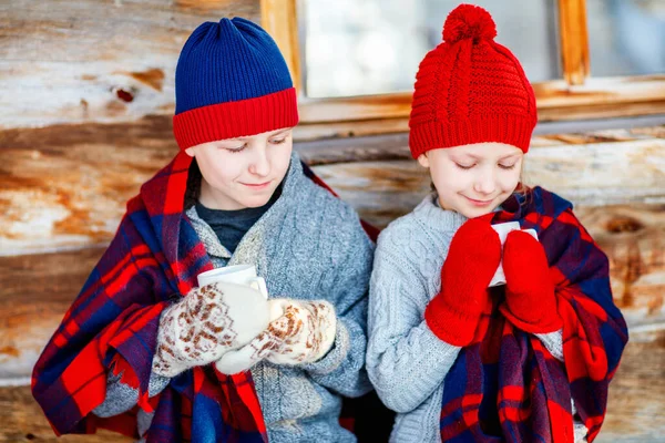 ログキャビンの休暇家の前でホットチョコレートを飲む美しい冬の日に屋外の子供たち — ストック写真