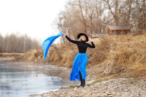 Full length view of blonde woman in hat posing outdoors by river