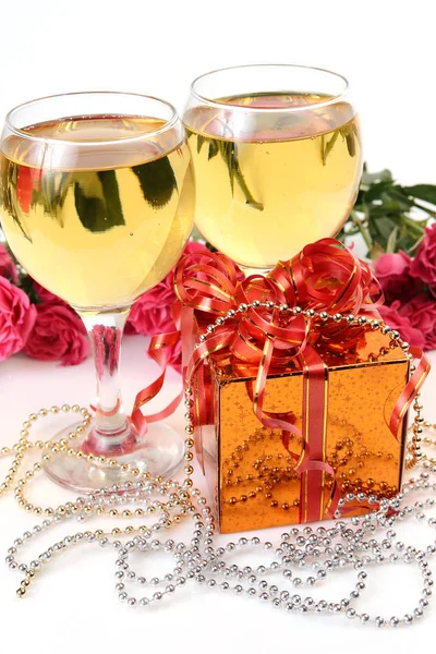 wine in glasses, box with bow, pink roses and beads on white background