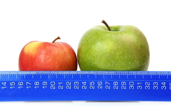 Dos manzanas verdes y rojas sobre un fondo blanco y una regla azul — Foto de Stock