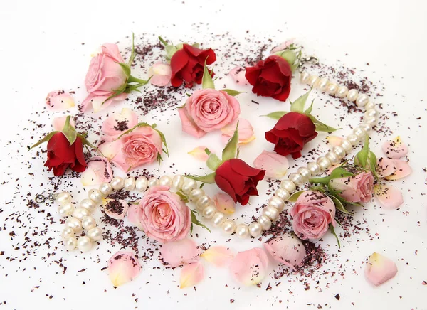 Pink and red roses scattered on surface with pearl beads