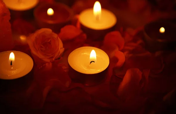 Rosenblätter und Kerzen, die im Dunkeln brennen — Stockfoto