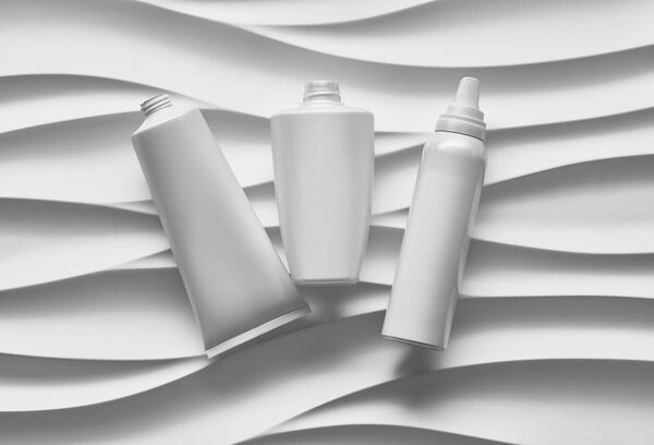 Красивый плакат формата с плавно-серыми волнами абстрактного фона с сероватыми тональностями, с чистыми белыми пластиковыми контейнерами: бутылки, банка крема, трубка. Реалистичный макет косметического пакета

