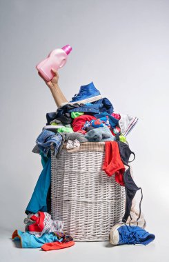 Tam Çamaşırhane gri arka plan üzerinde beyaz hasır sepet. Bir el çamaşır deterjanı pembe bir şişeyle tutar