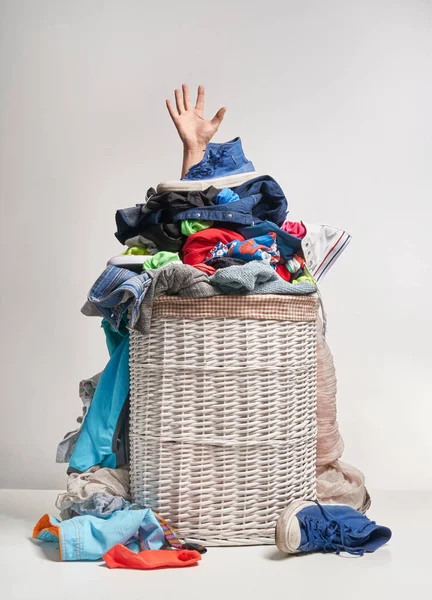 Full laundry white wicker basket, with a hand sticking out, on the grey background