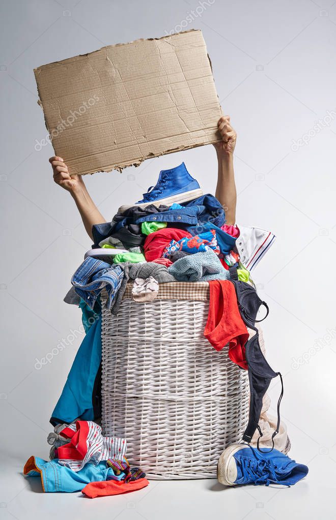 Full laundry white wicker basket on the grey background. Two hands hold a cardboard tablet
