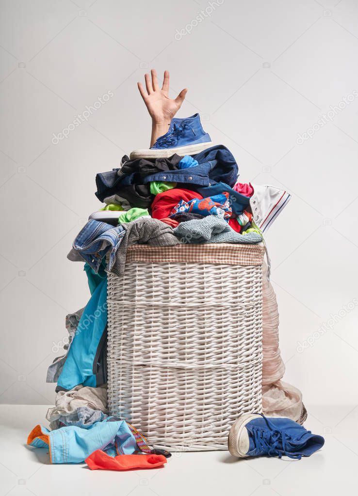 Full laundry white wicker basket, with a hand sticking out, on the grey background