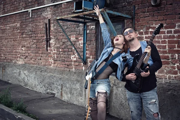 Girl and guy punks on a city street play on guitars