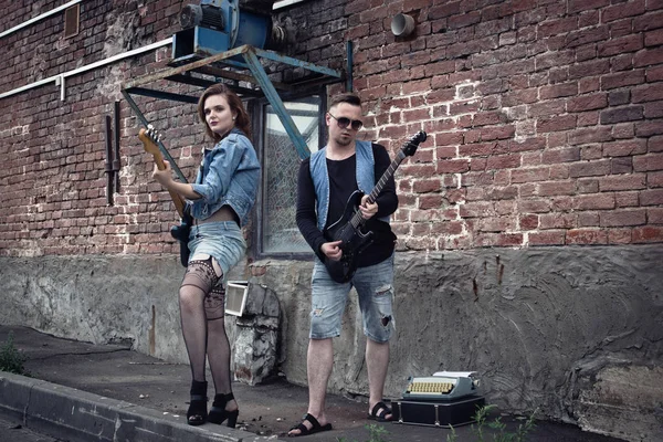 Girl and guy punks on a city street play on guitars