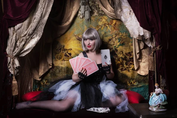 Pretty gothic girl with cards in a dark room interior