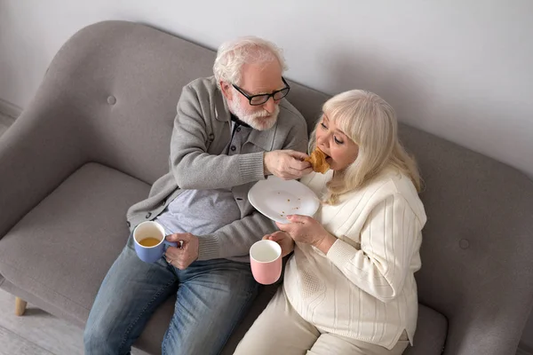 ソファでコーヒーを飲んでいる高齢者夫婦. — ストック写真