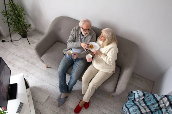 Aged couple having coffee on couch. — Stock Photo, Image