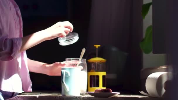 Mujer joven en la cocina poniendo azúcar en la taza con té . — Vídeo de stock