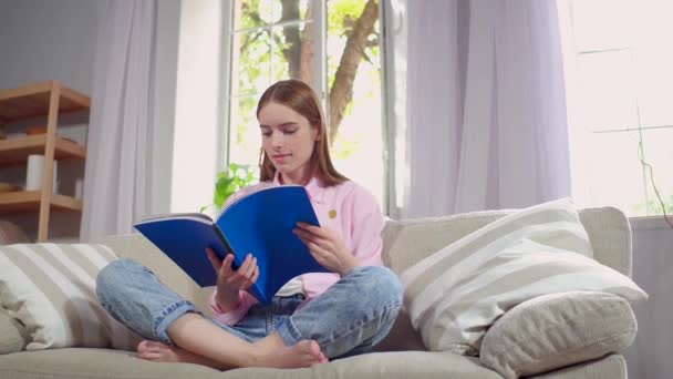 Fiatal nő ül a kanapén olvasó magazin. — Stock videók
