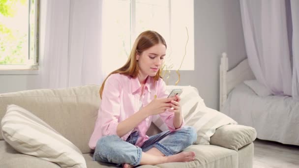 Blick auf charmantes Mädchen, das im Wohnzimmer auf dem Smartphone kommuniziert. — Stockvideo