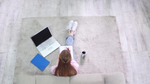 Вид сверху студентки, сидящей на ковре и пишущей в тетрадке . — стоковое видео
