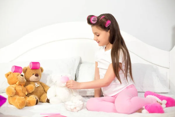 Menina bonito brincando com animais de pelúcia na cama . — Fotografia de Stock