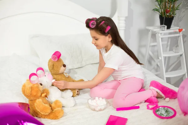 Menina bonito brincando com animais de pelúcia na cama . — Fotografia de Stock