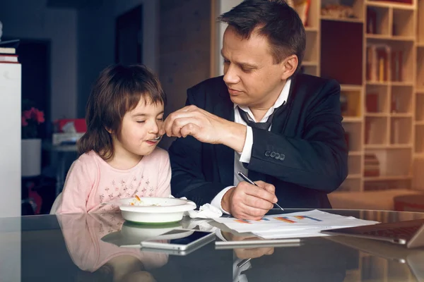 Far i kostym arbetar med papper och utfodring dotter — Stockfoto