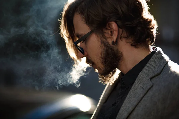 A man with long hair smokes outside — Stock Photo, Image